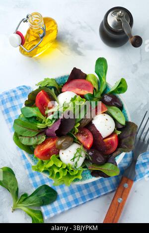 Fresh salad with lettuce, cress-salad, arugula, beets, tomatoes, mazarella cheese and olives in a ceramic mug on a light backgro Stock Photo