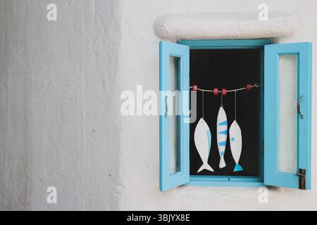 Pastel blue window with hanging fish mobile on white wall, Mediterranean style with copy space on the left. Minimal coastal home decor. Stock Photo