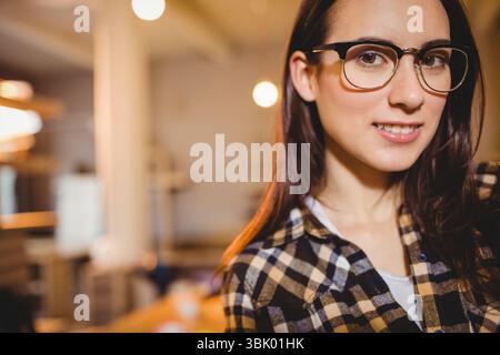 Woman wearing black-framed eyeglasses and checkered shirt in softly lit space with pendant lights Stock Photo