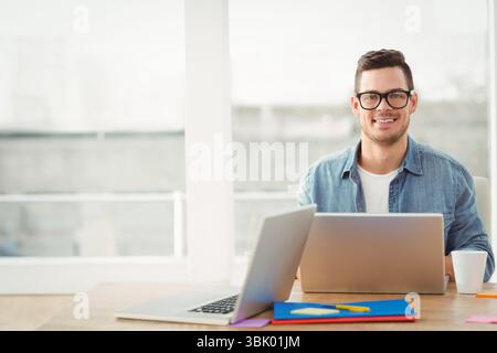 Two laptops resting on desk in bright home office near windows, with coffee mug and folders Stock Photo
