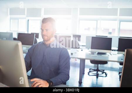 Computer monitor glowing on white desk with keyboard and mouse resting and chairs in bright lab Stock Photo