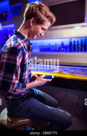 Smartphone glowing on reflective bar counter under neon blue lighting, with bottles in background Stock Photo