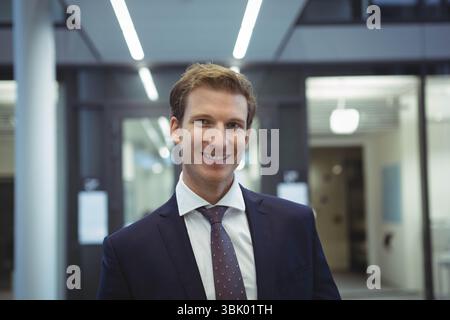 Businessman wearing navy suit jacket and burgundy tie standing under LED lights in office corridor Stock Photo