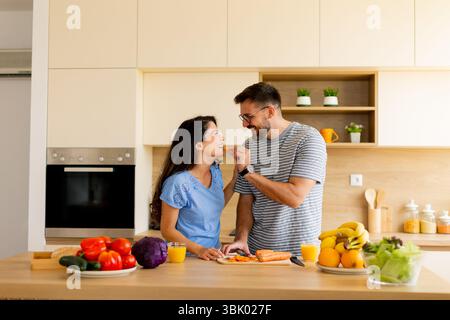 A couple enjoys each other's company while preparing a nutritious meal, surrounded by vibrant fruits and vegetables in a bright kitchen. Stock Photo
