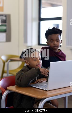 Diverse boys collaborating on laptop in classroom, focusing on project together, at school Stock Photo
