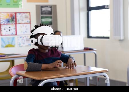 In school, african american boy using VR headset at desk, exploring virtual learning Stock Photo