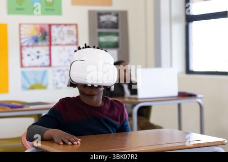 In school, african american boy using VR headset at desk, exploring virtual learning Stock Photo