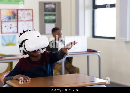 African american boy using vr headset in classroom, exploring virtual world, at school Stock Photo