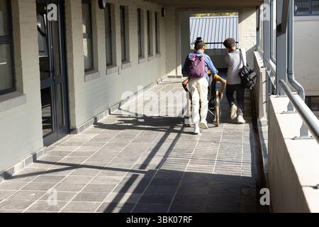 Walking in school hallway, diverse students with backpacks, one using wheelchair Stock Photo