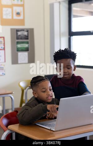Diverse boys collaborating on laptop in classroom, learning together with focus, at school Stock Photo