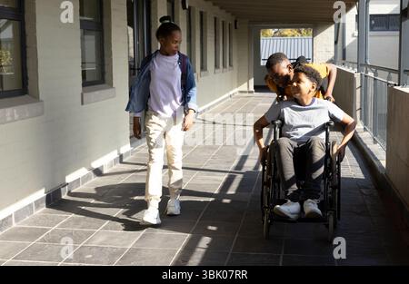 Walking together in school hallway, diverse students with wheelchair, having conversation Stock Photo