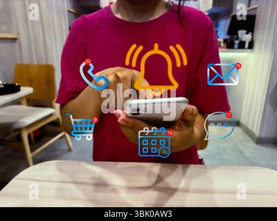 Notification Alert and Digital Communication Concept. Young entrepreneur checks smart phone with floating notification icons for messages, calls, emai Stock Photo