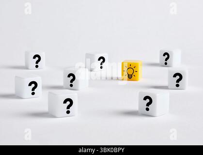 To find creative ideas and problem solving. Single yellow dice standing out with light bulb symbol printed, surrounded by question marks on white dice Stock Photo