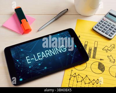 Digital tablet displaying an e-learning concept, laying on a desk with office supplies and a notepad with charts and diagrams. Stock Photo