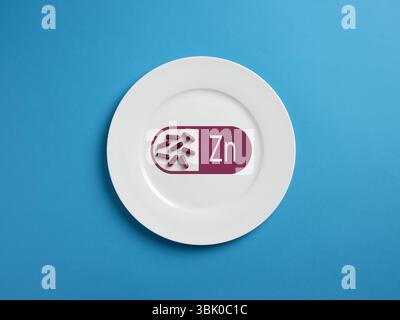 Zinc pills placed on white plate over blue background. Concept of zinc deficiency and treatment. Zinc supplement and healthy nutrition. Stock Photo