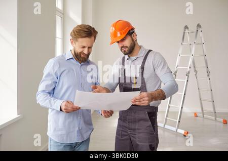 Architect in uniform and hardhat, holding house construction blueprint, talking with man client Stock Photo