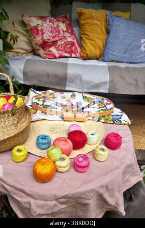 Close-up of a small garden table with embroidery supplies on a warm summer day. Colorful threads, needles, fabric, scissors, and a wooden hoop Stock Photo