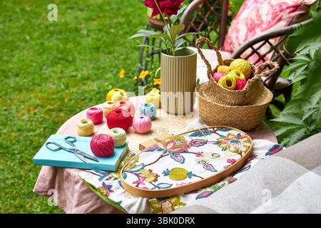 Close-up of a small garden table with embroidery supplies on a warm summer day. Colorful threads, needles, fabric, scissors, and a wooden hoop Stock Photo