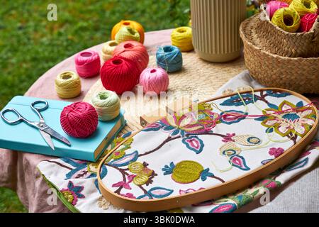 Close-up of a small garden table with embroidery supplies on a warm summer day. Colorful threads, needles, fabric, scissors, and a wooden hoop Stock Photo