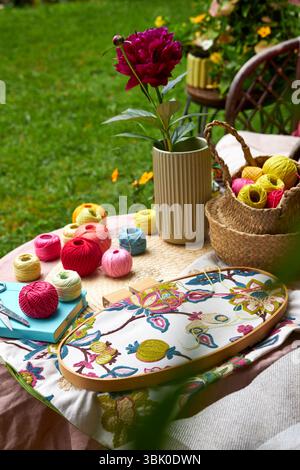 Close-up of a small garden table with embroidery supplies on a warm summer day. Colorful threads, needles, fabric, scissors, and a wooden hoop Stock Photo