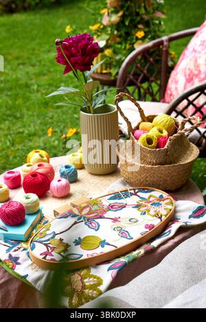 Close-up of a small garden table with embroidery supplies on a warm summer day. Colorful threads, needles, fabric, scissors, and a wooden hoop Stock Photo