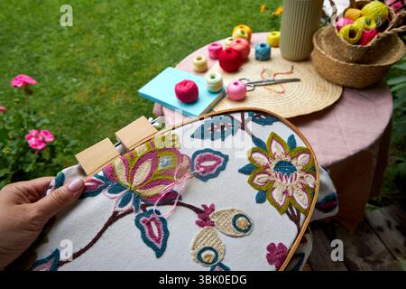 Front close-up view of a woman's hands embroidering a decorative pattern on fabric stretched in an embroidery hoop. The hands are focused and steady Stock Photo