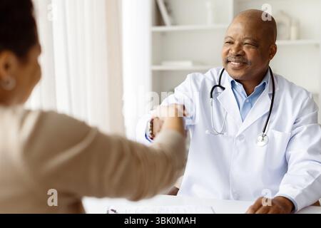 Friendly african american male doctor smiling and shaking female patient hand Stock Photo