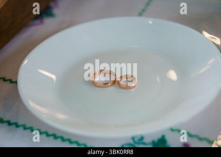 A close-up shot of two golden wedding rings resting on a white plate adorned with a colorful floral patterned tablecloth, representing commitment and Stock Photo