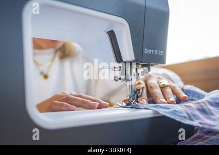 Sewing process with a sewing machine in a close-up, emphasised by the guiding hands with jewellery Stock Photo