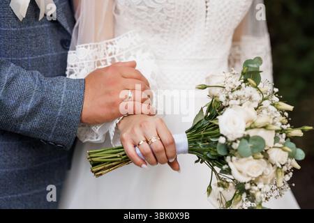 Intimate wedding scene showcases hands exchanging golden rings while holding a delicate white floral bouquet, symbolizing commitment and joyful celebr Stock Photo