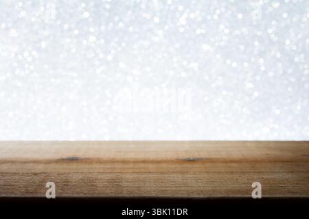 Empty wooden tabletop against a bright, white bokeh background. The sparkling light effect evokes a festive, wintery, or celebratory atmosphere. Stock Photo