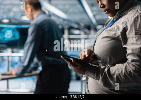 Close up of server room coworkers reviewing network configurations using software on tablet. Teamworking data center technicians tracking resource utilization trends using device Stock Photo