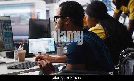 African american wheelchair user working in solar panel factory, optimizing systems for renewable energy. Engineer examines robot arms automation in a disability friendly power plant. Camera A. Stock Photo