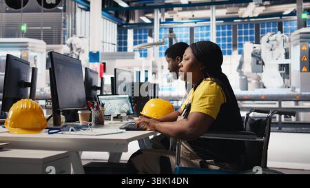 Photovoltaics factory engineer wheelchair user improving solar panels on an industrial software, working on computer for the manufacturing industry. Renewable energy. Camera B. Stock Photo