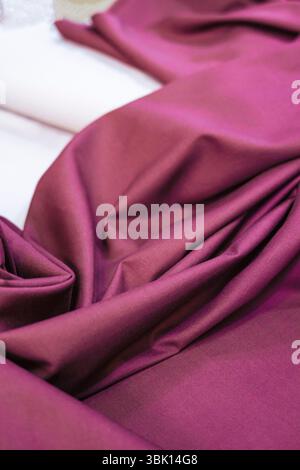 Close-up view of rich maroon fabric, showcasing its texture and drape. The folds and creases highlight the material's luxurious feel.  Perfect for des Stock Photo