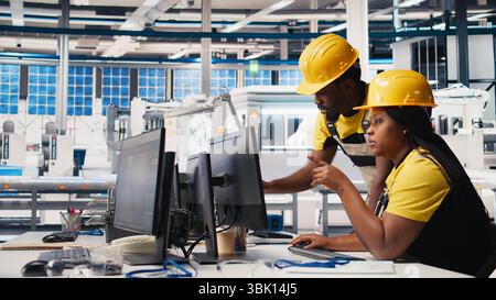 All black team of engineers comparing solar panels designs on devices, working on the production line at the manufacturing plant. Troubleshooting together and ensuring optimization. Camera B. Stock Photo