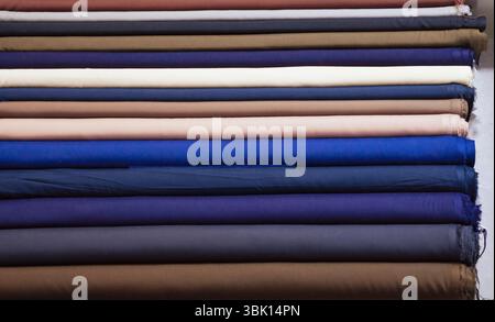 A close-up shot of numerous fabric rolls neatly stacked, showcasing a variety of colors and textures.  The rolls are tightly wound, displaying a range Stock Photo