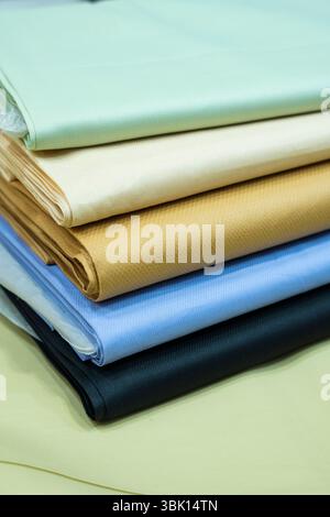 A close-up view of neatly stacked fabric swatches showcasing a range of colors including pastel green, beige, brown, light blue, and dark black. The t Stock Photo
