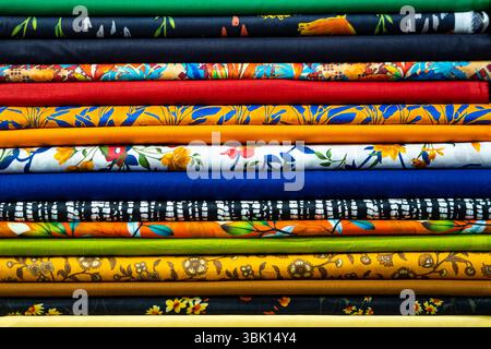The background is a simple, neutral setting. The foreground is dominated by a neatly stacked pile of colorful fabric rolls.  Each roll displays a diff Stock Photo