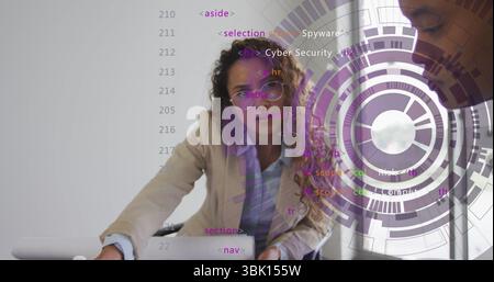 Woman wearing blazer leaning on office table pointing at laptop showing code and circular graphics Stock Photo