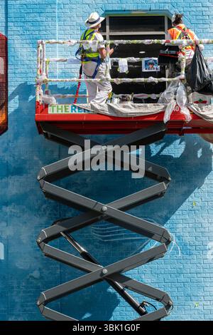 Two artists painting a colorful mural on a brick building while standing on a hydraulic lift. Downtown Calgary Alberta Canada Stock Photo