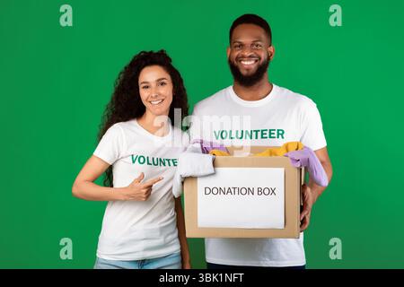 Two Volunteers Holding Donation Box Standing Over Green Background Stock Photo