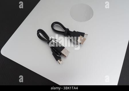 Two charging usb-c cables placed on silver laptop. . Stock Photo