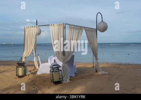Beach scene with a white tent and white curtains for the wedding. The tent is set up on the beach and has a table and chairs. The beach is calm and pe Stock Photo