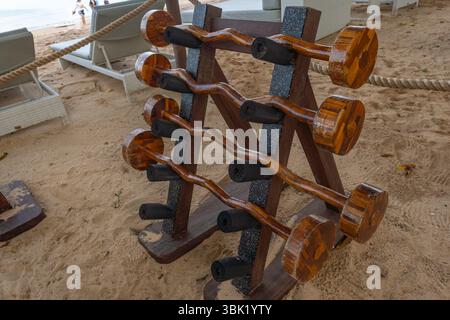 Wooden rack of dumbbells is on a sandy beach. The dumbbells are wooden and are stacked on top of each other Stock Photo