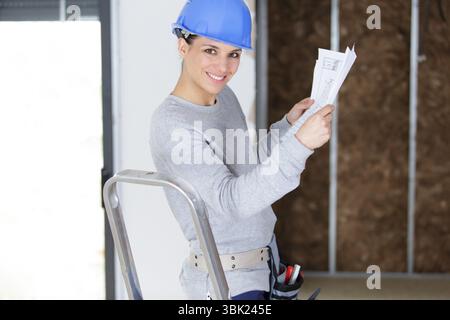 female architect looking at a plan standing on stepladder Stock Photo