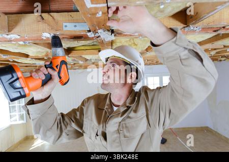 builder using cordless screwdriver on wooden ceiling joist Stock Photo