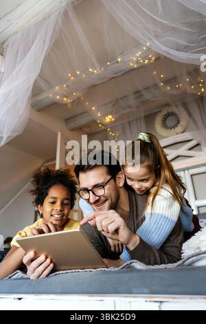 Excited single father plays with diverse, multi-ethnic daughters. Using digital tablet enjoy weekend Stock Photo