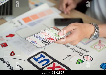 User Interface Design. Hand holding smartphone with app features during brainstorming session. Stock Photo
