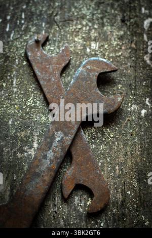 Two old wrenches rest crossed on a weathered wood surface, revealing their rust and signs of many years in mechanical work Stock Photo